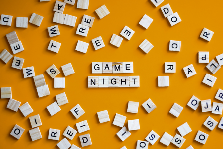 A yellow background with Scrabble tile pieces scattered around and the words Game Night written in Scrabble tiles