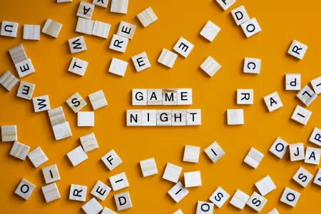 A yellow background with Scrabble tile pieces scattered around and the words Game Night written in Scrabble tiles