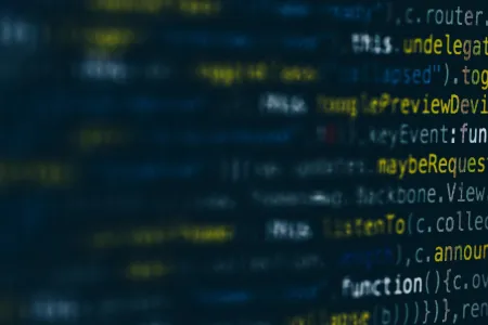 A blurred background of computer code and text in dark blue, white and yellow font. 